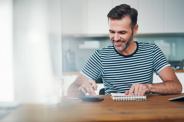 smiling man using notebook and calculator to manage home budget - home finances calculator currency finance imagens e fotografias de stock