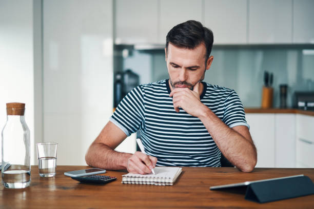 istock Thoughtful man looking at notebook while sitting at home managing personal budget 1169342473