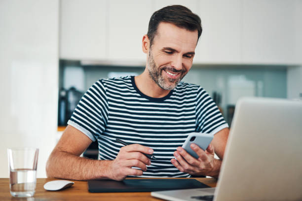 Happy web designer looking at smartphone while taking break from working in home office