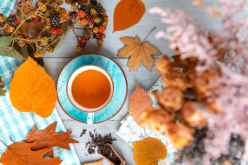 composition still life of a mug with hot leaf tea with berries and autumn leaves on a wooden surface