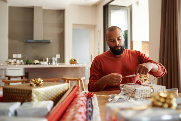 He's got gift wrapping duties covered Shot of a young man wrapping Christmas presents at home wrapped stock pictures, royalty-free photos & images