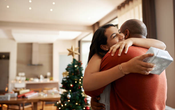 Christmas is a time of giving Shot of a happy young couple exchanging Christmas gifts at home unwrapping stock pictures, royalty-free photos & images