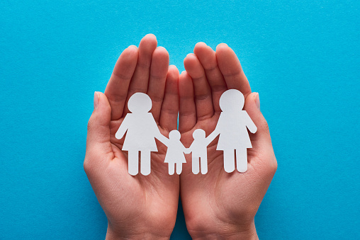 cropped view of woman holding paper cut lesbian family near on blue background