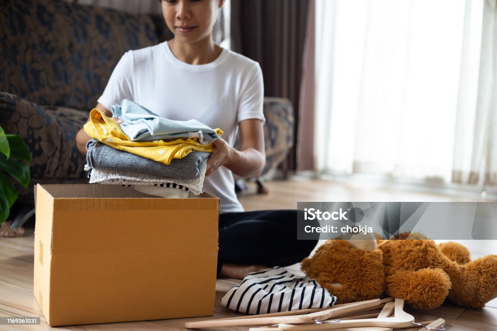 Woman holding Clothes with Donate Box In her room, Donation Concept. Clothing Stock Photo