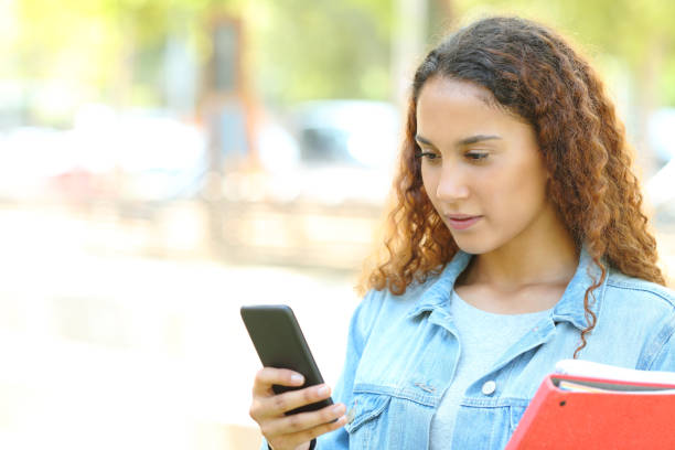 istock Serious mixed race student checking phone in a park 1169370625