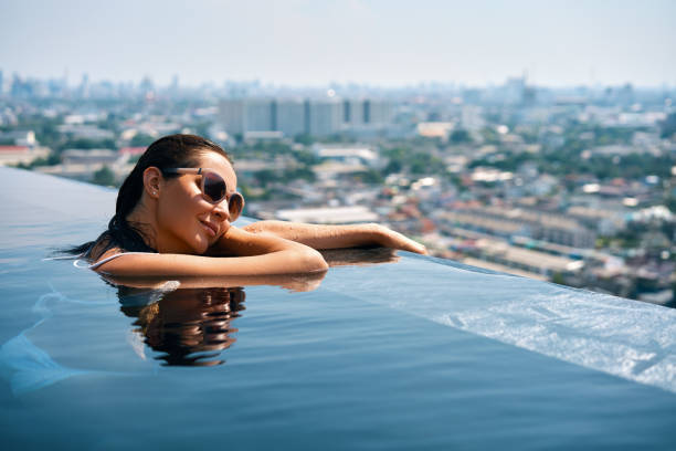 молодая женщина отдыхает на краю бассейна на крыше - poolside enjoyment sensuality blue стоковые фото и изображения