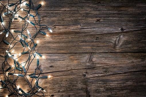 Top view of an empty rustic wooden table with Christmas lights string arranged at the left border making a frame and leaving useful copy space for text and/or logo at the right. Predominant colors are brown and yellow. XXXL 42Mp studio photo taken with SONY A7rII and Sony FE 90mm f2.8 Macro G OSS lens