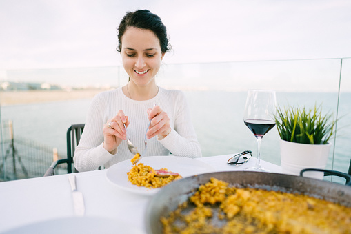 Happy tourist woman in restaurant eating traditional paella
