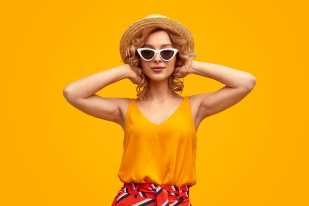 Trendy lady adjusting hair Pretty female hipster in stylish outfit looking at camera and adjusting wavy blond hair against vivid yellow background personal accessory photos stock pictures, royalty-free photos & images