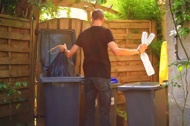 Man putting plastic bottles in a yellow container and garbage in a bag in a green container