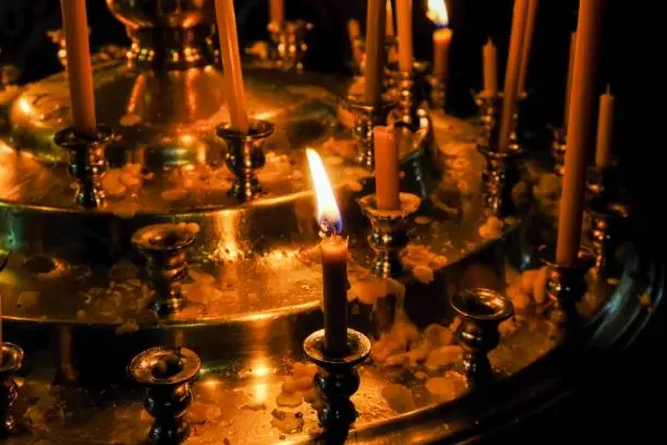 Thin funeral candles burn in front of holy images in an Orthodox Christian church close-up