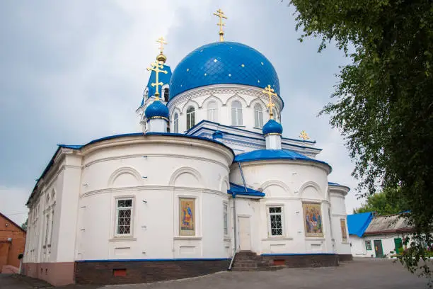 Christian Church of white stone with blue domes with stars and gold crosses. Holy Trinity Church in Tomsk, Russia.