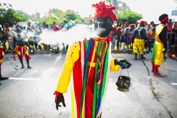 Dominican Republic, Punta Cana - March 3, 2018: Haitian Voodoo shaman blows smoke from his mouth and carries fire. Face painted with national colors. The annual parade.