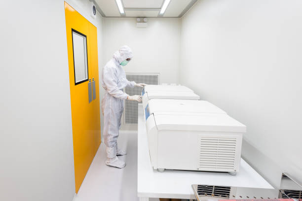 A scientist in sterile coverall gown using laboratory equipment for doing biological research in cleanroom. stock photo