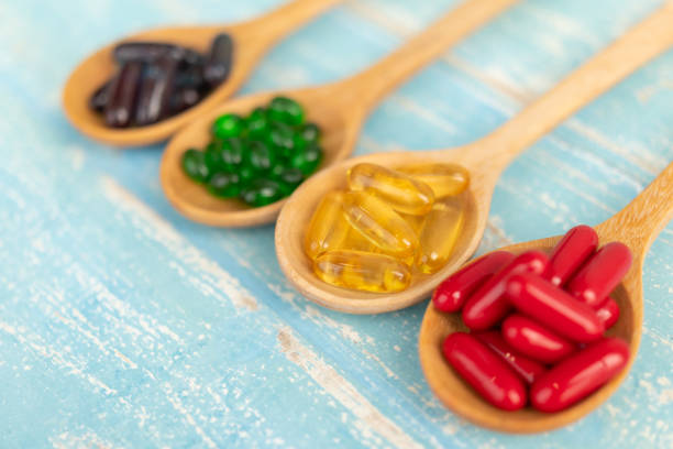 Close-up of supplements on a blue background Close-up of colorful soft gelatin capsule supplements in a wooden spoon on a blue background Vintage. Soft Gel stock pictures, royalty-free photos & images