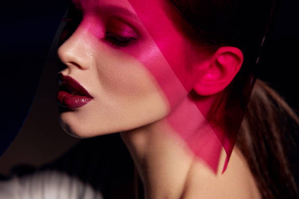 Makeup beauty. Woman model with dark lipstick under pink light. Closeup portrait of glamorous girl with beautiful sexy make-up, lip gloss and glowing skin under color lights. High quality image