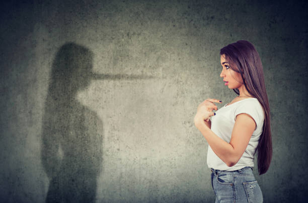 woman pointing at herself looking at a shadow with long nose of a liar. Side view of a woman pointing at herself looking at a shadow with long nose of a liar. hypocrisy stock pictures, royalty-free photos & images