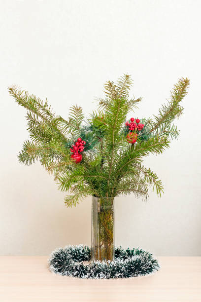 istock Christmas tree branches with red decorations with balls in a vase on a beige background. Vertical view 1169418715