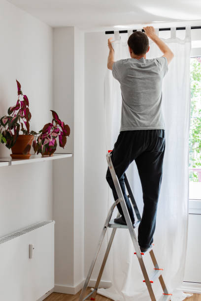 istock Man hangs white curtains on the curtain rod 1169430396