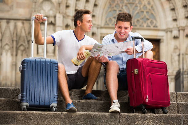 Positive couple men sitting at stairs with map and baggage