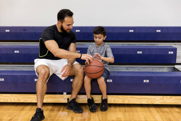 le père et le fils s'asseyaient sur des gradins de gymnastique et parlent de basket-ball - sport parent bleachers family photos et images de collection