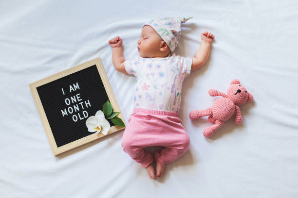 Portrait of sleeping one month old newborn baby girl laying between letter board and teddy bear. Flat lay composition. Cute one month old newborn baby girl in trendy outfit laying between letter board and teddy bear. Shot from overhead on white background. Flat lay composition. teddy bear photos stock pictures, royalty-free photos & images