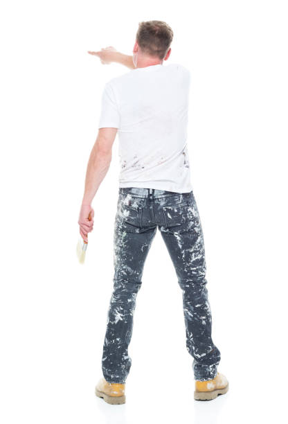 istock Young male painter with stained clothes on white background - rear view, pointing / touching 1169444588