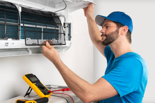Installation service fix  repair maintenance of an air conditioner indoor unit, by cryogenist technican worker checking the air filter in blue shirt baseball cap stock photo