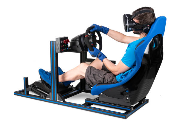gamer in blue tshirt with VR virtual reality glasses training on simracing aluminum simulator rig for video game racing. Motorsport car bucket seat steering wheel pedals isolated white background gamer in blue tshirt with VR virtual reality glasses training on simracing aluminum simulator rig for video game racing. Motorsport car bucket seat steering wheel pedals isolated on white background gaming chair photos stock pictures, royalty-free photos & images