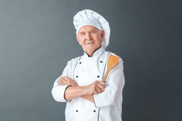 istock Senior chef studio standing isolated on gray holding spatula crossed arms looking camera proud 1169460228