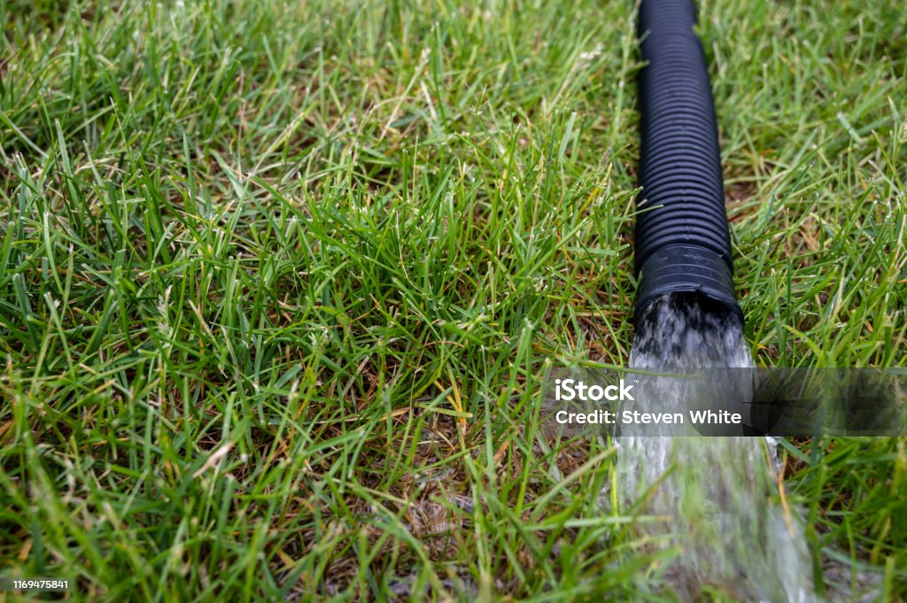 residential sump pump discharging water from the end of a flexible black hose draining water from structure, generally accomplished with a pump or suction Water Pump Stock Photo