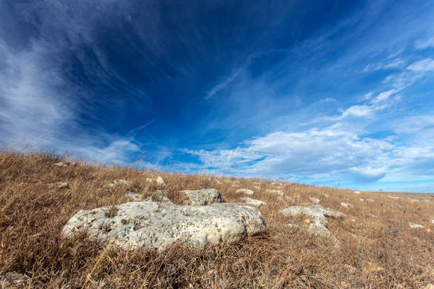 limestone rocks on brown grass hillside, cirrus clouds in blue sky; Kansas