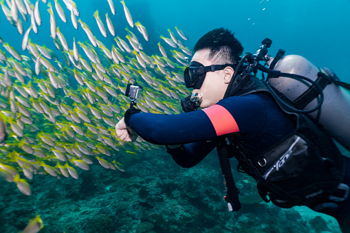 Phi Phi island, Thailand - July 22 2019:  One Chinese man in his 20’s is scuba diving underwater.  He has an underwater wearable action camera on his wrist and is filming the environment.  Cameras such as these are often used for travel blogs or vacation videos.