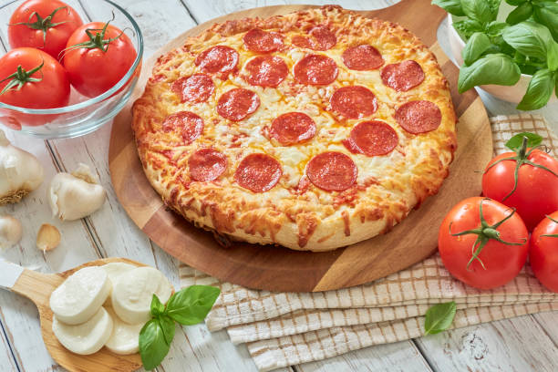 Pepperoni pizza Freshly baked pepperoni pizza on wooden tray, surrounded by natural fresh ingredients (mozzarella, basil, garlic and tomato). Photography made with natural day light. pepperoni pizza stock pictures, royalty-free photos & images