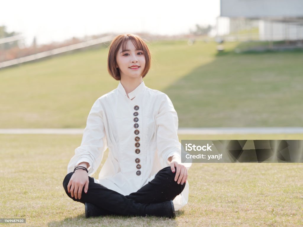 Schöne junge brünette Frau im weißen Hemd sitzt auf Wiesen mit Bein gekreuzt und lächelnd in der Kamera an sonnigen Tag. Outdoor-Mode-Porträt von Glamour chinesischen fröhliche stilvolle Mädchen. - Lizenzfrei Frauen Stock-Foto