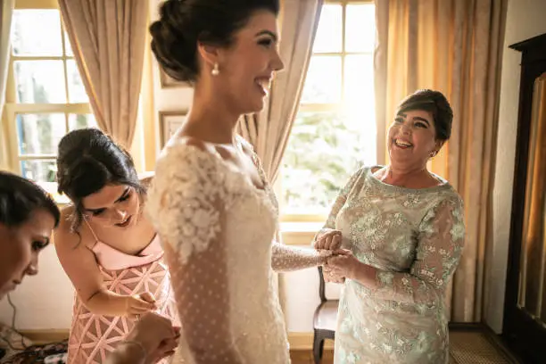 Photo of Bridesmaids helping bride getting dressed for the wedding ceremony