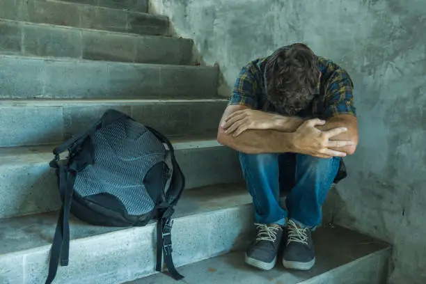 Photo of anti sexual discrimination and against homophobia campaign. Young sad and depressed college student man sitting on staircase desperate victim of harassment suffering bullying and abuse