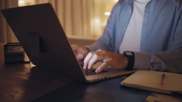 Close-up of a man working from home typing on laptop till late night