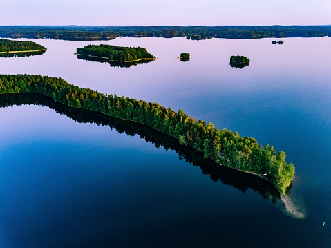 Aerial view of blue lakes with islands and green forests on a summer day in Finland.