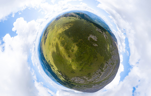 Aerial view of planet earth in the form of a nutlet with the image of nature and picturesque landscapes near a mountain with a rocky peak on a summer day with white clouds and blue sky. A small and defenseless planet.