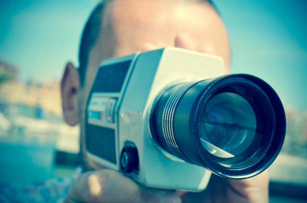 young man filming with a retro film camera closeup of a young caucasian man filming with a retro film camera outdoors vintage amateur movie camera stock pictures, royalty-free photos & images