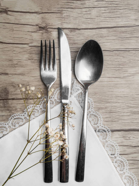 istock Light colored tableware set: vintage silverware on napkin and delicate white flowers on wooden background with copy space. 1169519819