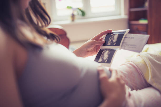 giovane donna incinta che esamina la sua ecografia - ultrasound gynecologist gynecological examination human pregnancy foto e immagini stock