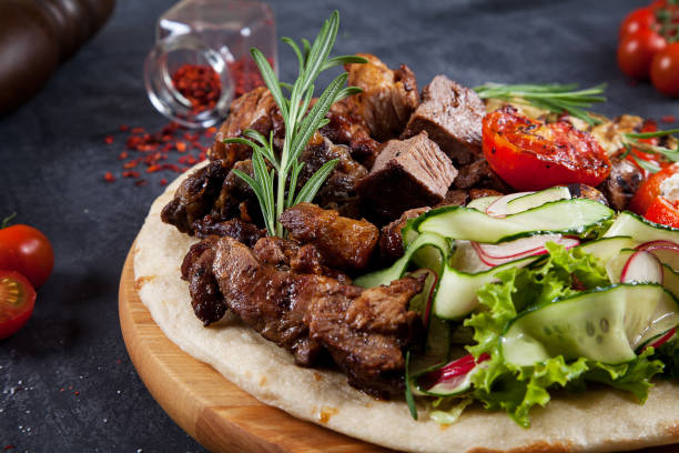 Close up view on tasty grilled meat with vegetables on georgian pita. shashlik or barbecue meat on pita. Shish kebab, traditional georgian cuisine food. Copy space for design. Dark background stock photo