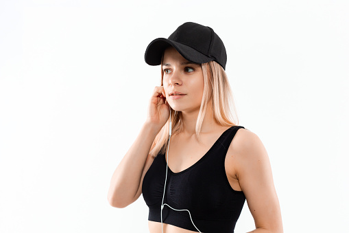 Young sporty blond woman in a black sportswear with smart watches listens to music during workout standing over white background. Listening to music during sport training.