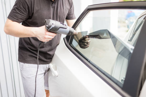 Worker removing car window film foil by using hot air gun.