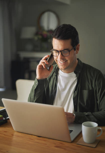 Happy man talking on mobile phone while using laptop at home