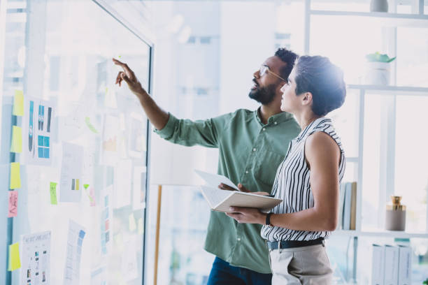 Managing their newest creative campaign Shot of two businesspeople brainstorming with notes on a glass wall in an office transparent wipe board stock pictures, royalty-free photos & images