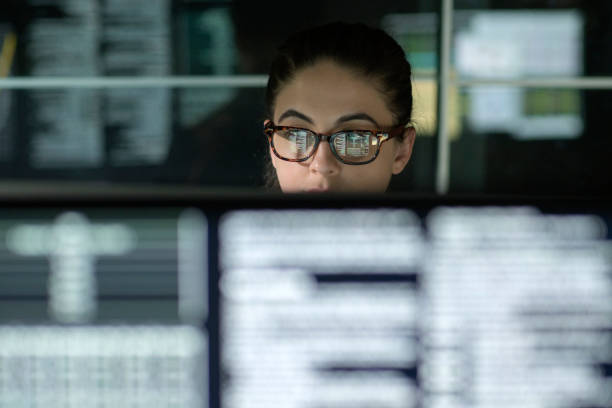 Data woman monitors A young woman is surrounded by monitors & their reflections displaying scrolling text & data. woman trading stocks stock pictures, royalty-free photos & images