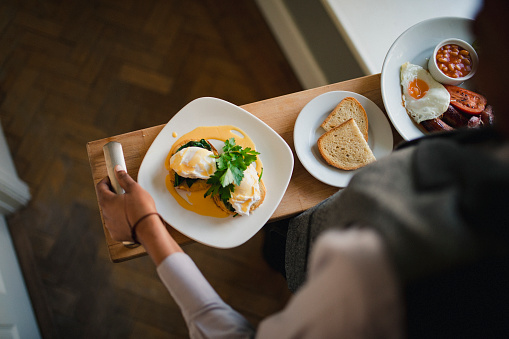 A waiter is walking while holding a breakfast tray with a full English breakfast and poached eggs on toast covered in Hollandaise sauce on it.